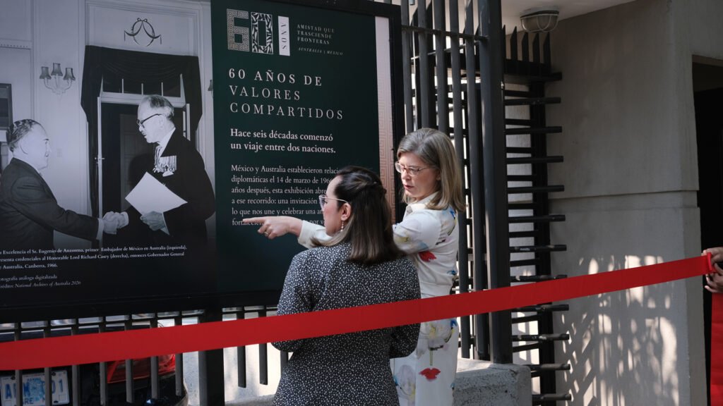 Rachel Moseley, embajadora de Australia y Ximena Gómez Chávez, directora del Sudeste Astático de la SRE frente al primer cartel en blanco y negro, que muestra el establecimiento oficial de las relaciones diplomáticas entre México y Australia. El saludo es durante la presentacion de las cartas credenciales deEugenio de Anzorena, (pimer embajador de Mexico en Australia) al entonces Gobernador General de Australia, Lord Richard Casey.